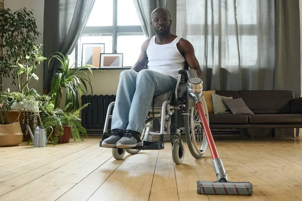 アフリカの若い男が車椅子に座って 自宅でリハビリ中に掃除機で家事をする — ストック写真