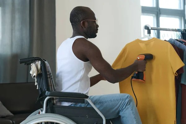 Африканский Юноша Сидящий Инвалидном Кресле Используя Пароход Погладить Одежду Висящую — стоковое фото