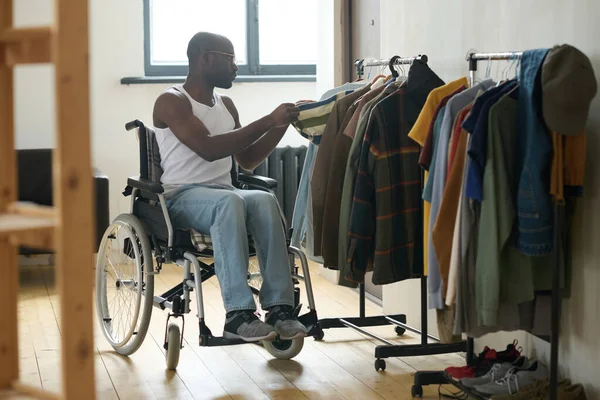 車椅子に座って障害のあるアフリカ人男性とラックにぶら下がって着る服を選ぶ — ストック写真