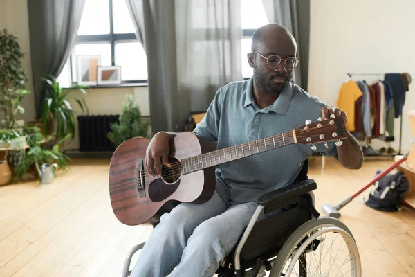 アフリカ系アメリカ人の障害者が車椅子に座り 自宅で音楽を演奏するためのギターをチューニング — ストック写真