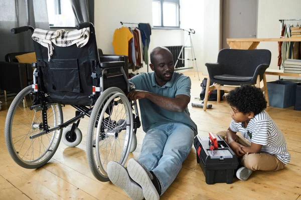 Африканський Хлопчик Сидить Підлозі Кімнаті Скринькою Допомагає Батькові Інвалідністю Ремонтувати — стокове фото