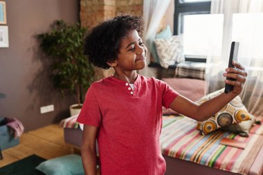 Önünde cep telefonu tutan Afrikalı bir çocuk ve odasında durup video içeriği çeken bir çocuk.