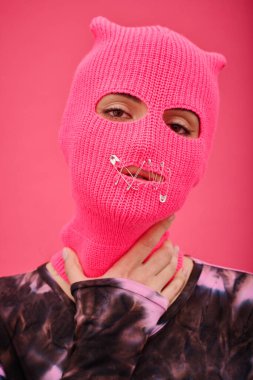 Pembe kar maskesi takan, ağzı dikilmiş ve konuşma hakkı olmayan genç bir kadının portresi.
