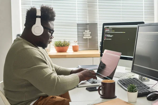 stock image African IT programmer in wireless headphone concentrating on his online work on laptop, he writing computer codes to program