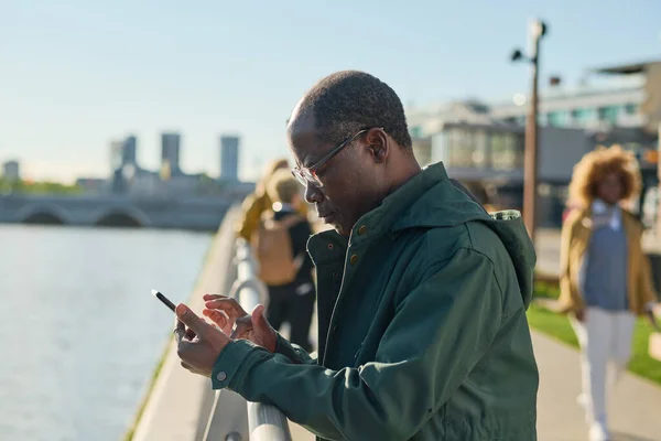 街の外に立っている彼の携帯電話にメッセージを入力する眼鏡のアフリカの成熟した男 — ストック写真