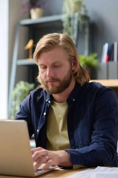 Young bearded office worker in casual using laptop for online work sitting at office desk