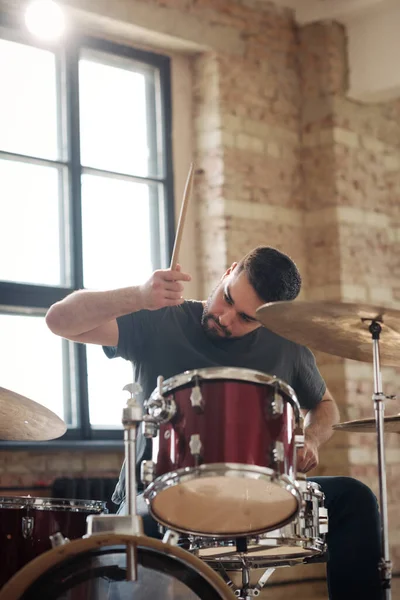 stock image Young professional drummer playing drums with drumsticks sitting at drum kit, he performing at musical studio