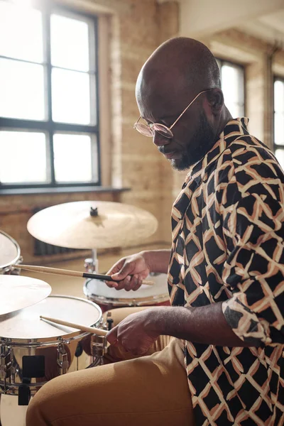 stock image African man in eyeglasses using drumsticks to play drums during practice at studio