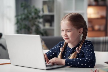 Dizüstü bilgisayara bakan ve evde online ders çalışan sevimli küçük kız.