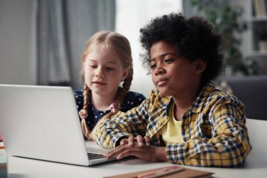 İnternetteki video görüşmesi sırasında laptopun önünde oturmuş monitöre bakan iki çocuk.