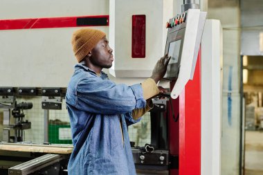Fabrikada ürün yapmadan önce program seçmek için makinenin monitörüne dokunan Afrikalı genç işçi