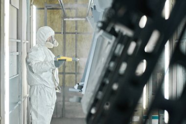 Fabrikadaki metal detayları boyamak için sprey tabanca kullanan koruyucu iş elbisesi sanayicisi.