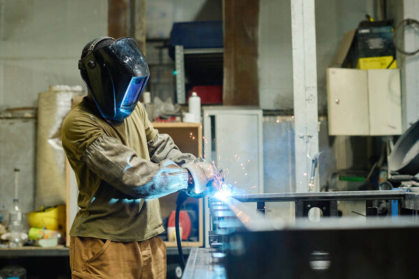 Welder in mask using torch to cut iron at his workplace in workshop