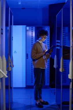 BT kadın teknisyeni sunucu kabinesinde dururken çevrimiçi veri yazma tableti üzerinde çalışıyor