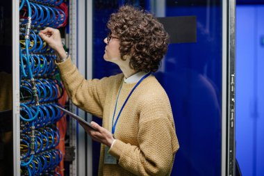 Sunucu odasındaki işi sırasında tablet bilgisayar kullanan ve raftaki internet kablolarını kontrol eden yazılım mühendisi