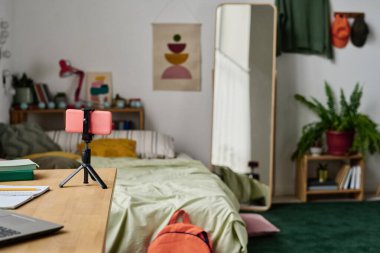 Tripodun üzerinde duran akıllı telefonun yatay görüntüsü yatak odasında çevrimiçi yayına hazırlanıyor.