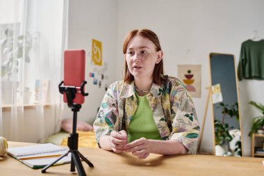 Blogcu kız, takipçileriyle internette konuşuyor. Odasında akıllı telefonuyla oturuyor.