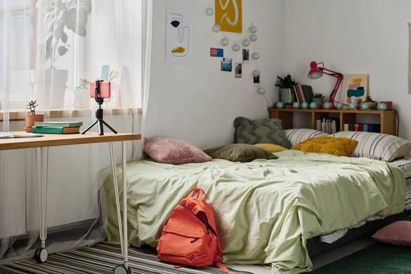 三脚の上にスマートフォン付きの居心地の良いベッドとテーブル付きの十代の部屋の水平画像 — ストック写真