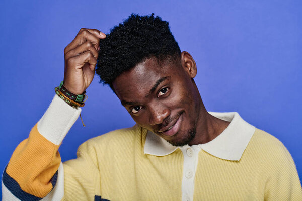 Портрет африканского юноши в яркой рубашке с браслетами на руке, позирующего перед камерой на синем фоне