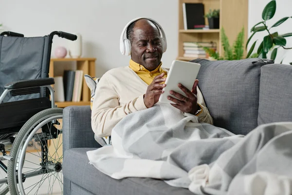 Африканский Взрослый Мужчина Инвалидностью Лежит Диване Одеялом Цифровым Планшетом Помощью — стоковое фото