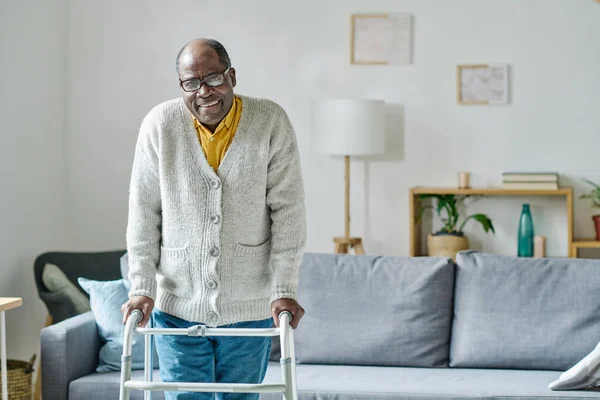 stock image Portrait of African senior man with disability smiling at camera while learning to walk with walker in the room