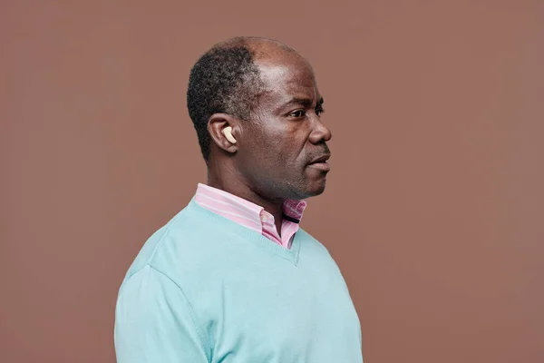 Side view of African senior man with hearing aid in his ear isolated on beige background