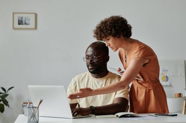 Genç iş kadını bilgisayarın monitörünü işaret ediyor ve ofisteki meslektaşıyla online sunumu tartışıyor.