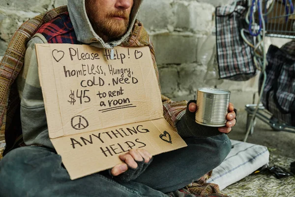 ポスターで屋外の地面に座っている貧しい男のクローズアップと生活のためのお金を求める — ストック写真