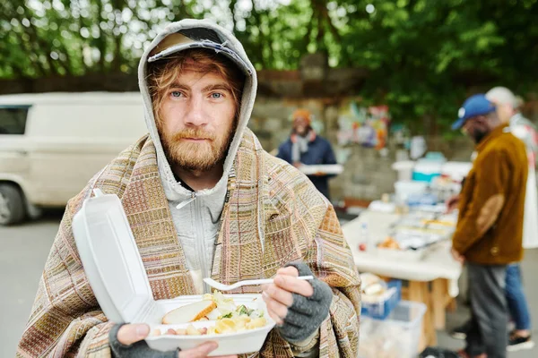 慈善事業中に屋外で食べ物を食べながら暖かい服を着た髭のホームレスの男の肖像画 — ストック写真