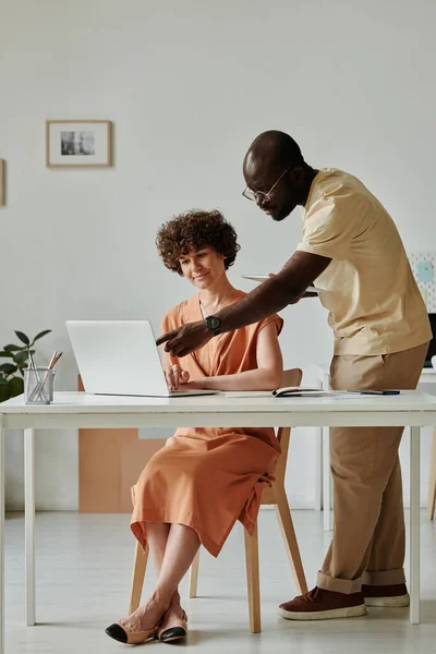 stock image African businessman pointing at monitor of laptop and discussing online project with his colleague