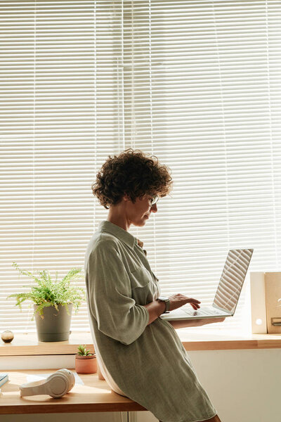 Young businesswoman leaning on her office desk and typing on laptop, she communicating online