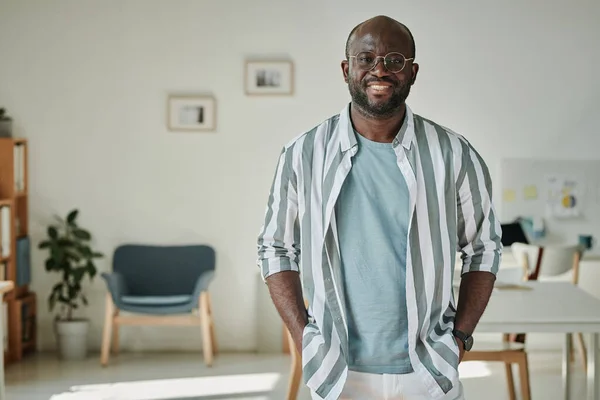 現代のオフィスに立ってカメラでカジュアルな笑顔でアフリカの若いビジネスマンの肖像画 — ストック写真