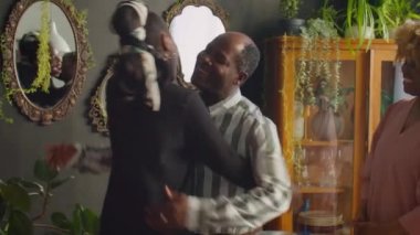 Neşeli Afrikalı Amerikalı çift, aile yemeği için toplanırken misafirleri kucaklıyor ve tokalaşıyor.