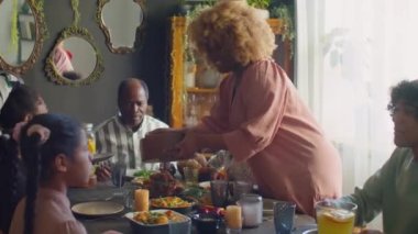 Afro-Amerikalı kadın aile yemeği yerken aile tabağına salata koyuyor.