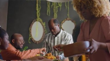 Afro-Amerikalı kadın aile fertleri için tabağa salata koyup evde yemek yiyor.
