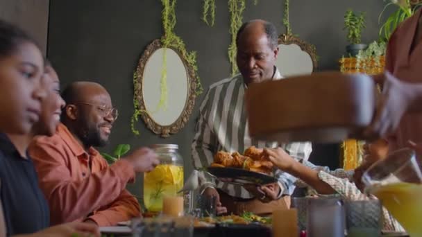 陽気なアフリカ系アメリカ人男性家族の家のディナーでゲストにフライドチキンを与える — ストック動画