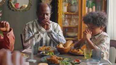 Afro-Amerikan ailesi yemekten önce evde birlikte yemek yerken gözleri kapalı dua ediyorlar.