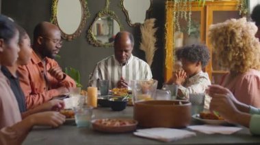 Büyük bir Afro-Amerikan ailesi babalarını dinler ve evde tatil yemeği yemeden önce gözleri kapalı dua ederler.