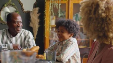 Küçük Afrikalı Amerikalı çocuk aile yemeğinde sevgi dolu ebeveynlerle sohbet ediyor.
