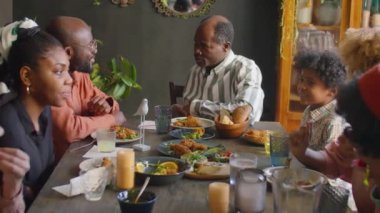 Neşeli Afro-Amerikan ailesi evde toplanırken bayram yemeğinde sohbet ediyorlar.