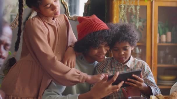 年轻的非洲裔美国男孩和快乐的哥哥姐姐坐在一起 在家里吃饭的时候笑着玩着数码平板电脑 — 图库视频影像