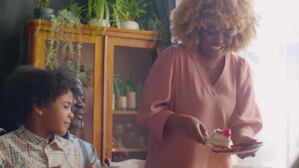 陽気アフリカ系アメリカ人女性置く甘いケーキ上のプレートのために家族のために休日の家の夕食 — ストック動画