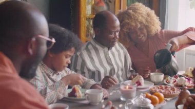Afro-Amerikalı bir kadın, aile için sıcak çay dolduruyor. Akşam yemeği partisinde doğum günü pastası yiyorlar.