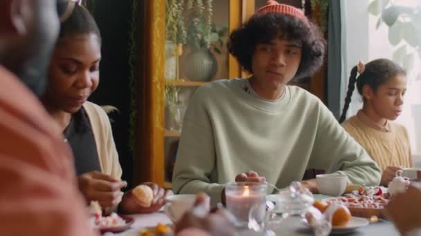 アフリカ系アメリカ人の10代の男の子がケーキを食べ お茶を飲み 休日の家の夕食で家族とチャット — ストック動画