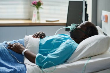 Hastane koğuşunda yüzünde oksijen maskesi olan Afro-Amerikalı baygın bir adam yatıyor.