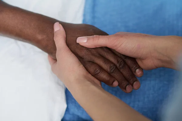 高齢のアフリカ系アメリカ人男性と手を取り合い 彼の病気の間に彼を支援する若い看護師のクローズアップ — ストック写真