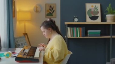 Down sendromlu beyaz bir kızın evde sentezleyici çalması.