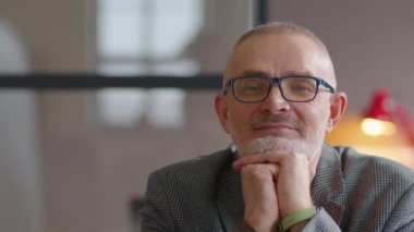 Gri saçlı ve sakallı neşeli kıdemli işadamının görüntüsü. Çenesi elleri dinleniyor ve ofiste kameraya poz veriyor.