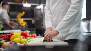 Mutfak masasında salatalık kesen tanınmamış bir restoran şefinin el kesimi. Meslektaşı arka planda yemek yerken.