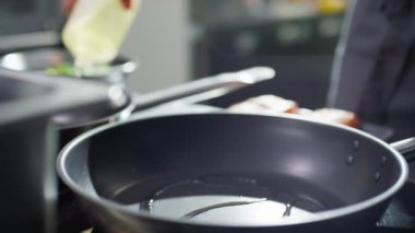 Erkek aşçının somon filetosunu diliyle tavaya koyduğu yakın plan.